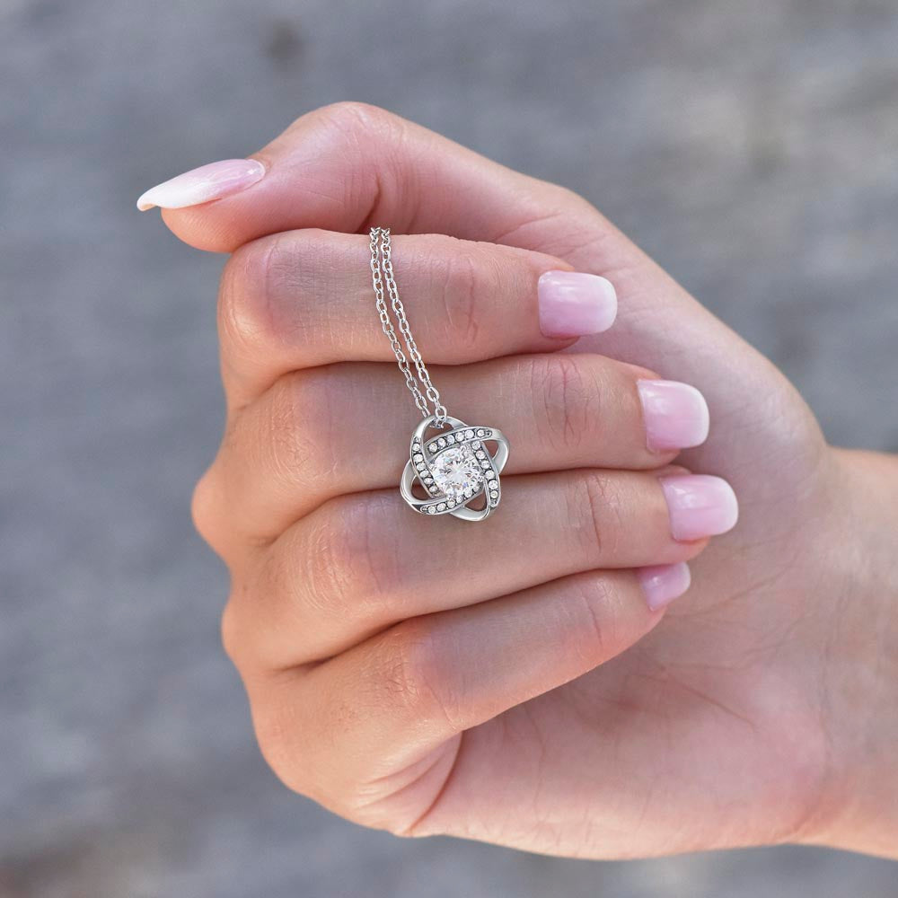 Love knot pendant held in the palm — size reference