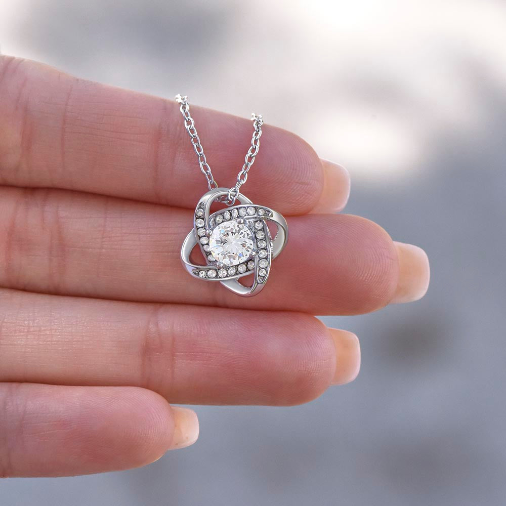 Love knot pendant held in the palm — size reference
