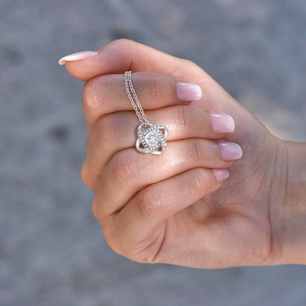 Love knot pendant held in the palm — size reference